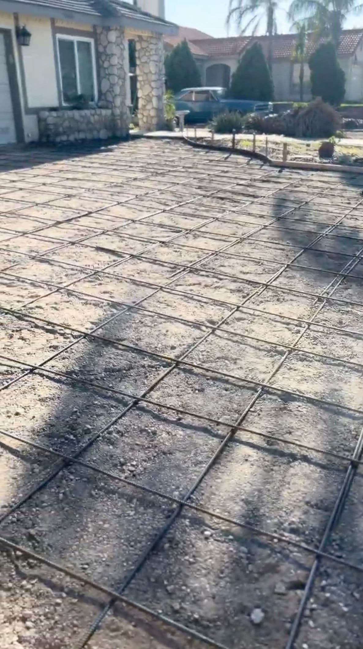 Concrete driveway preparation with rebar grid before pouring concrete. Sunny outdoor setting.